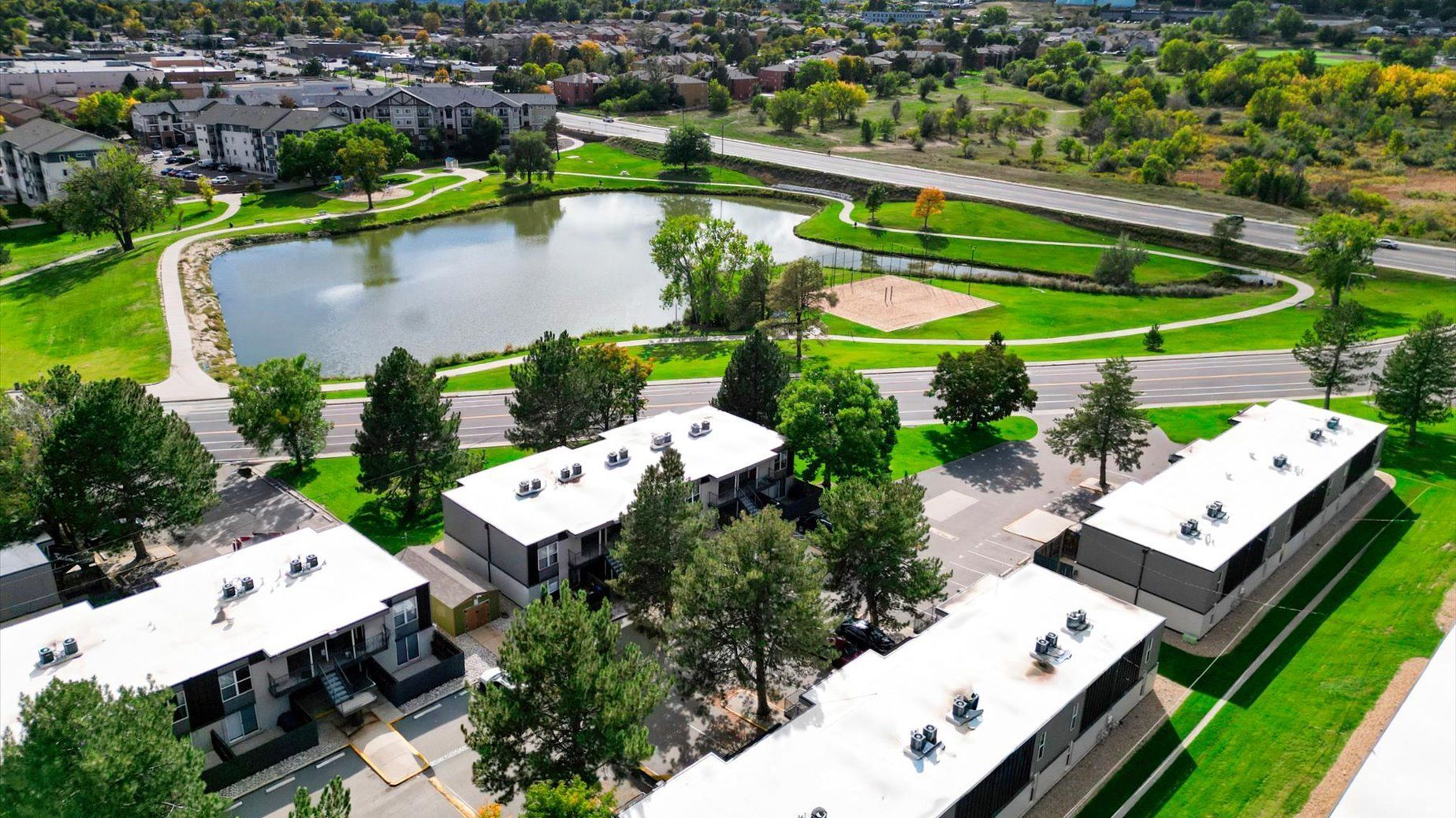 Aerial view of a residential community with a pond, green lawns, and walking paths among buildings.