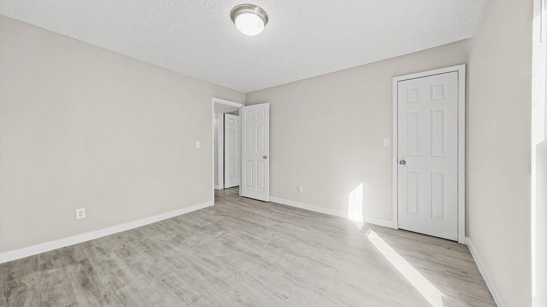 Empty beige room with white trim, laminate flooring, and two interior doors.