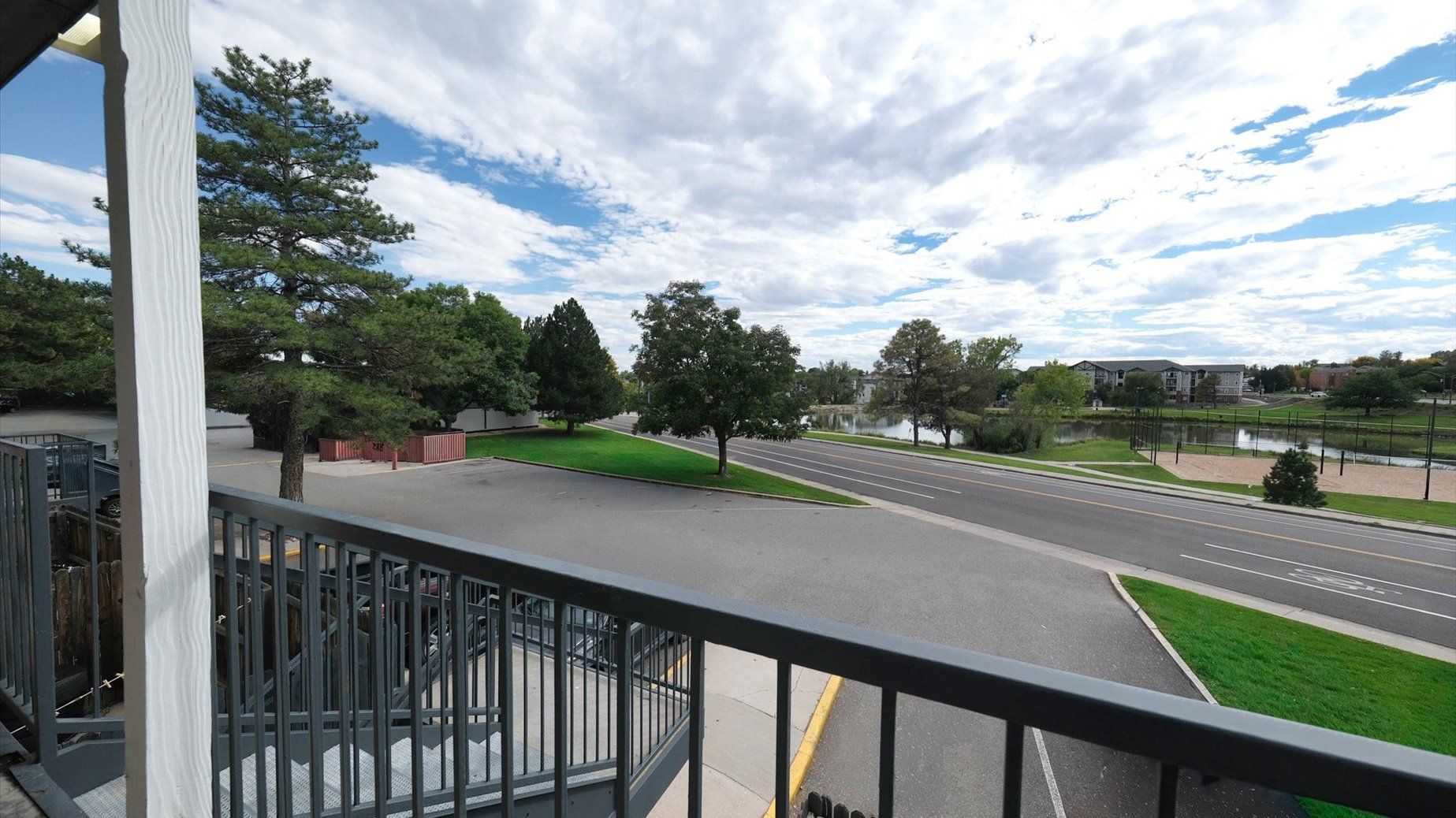 Balcony view of the property's outdoor grounds with trees, a road, and a pond.