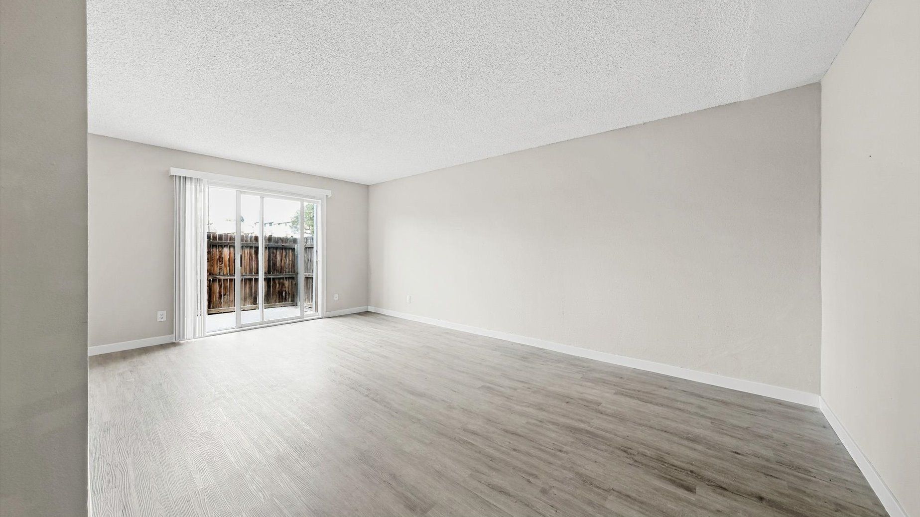 Empty living room with sliding glass door to a fenced outdoor area.