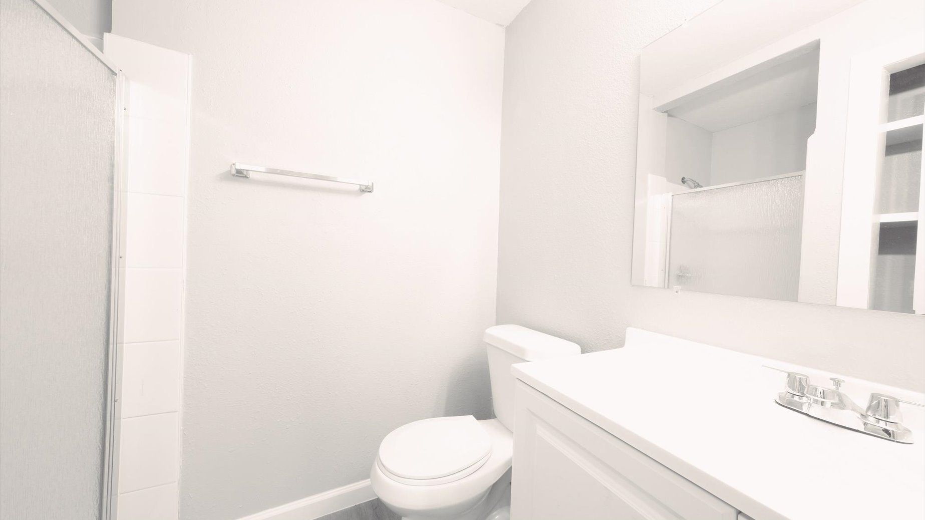 White bathroom with a vanity, mirror, toilet, and shower enclosure.