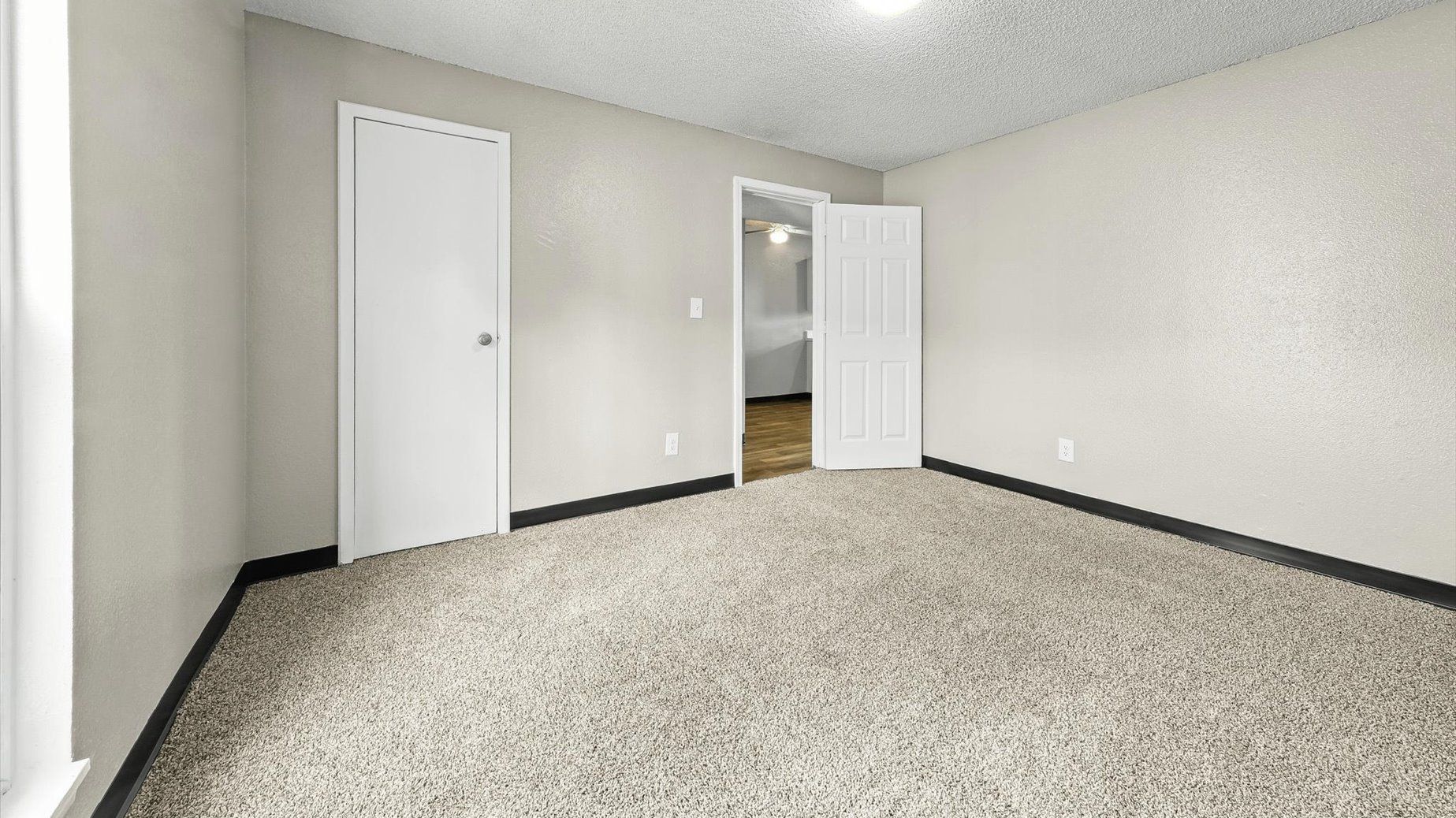 Vacant apartment room with beige walls, carpet, and a doorway.
