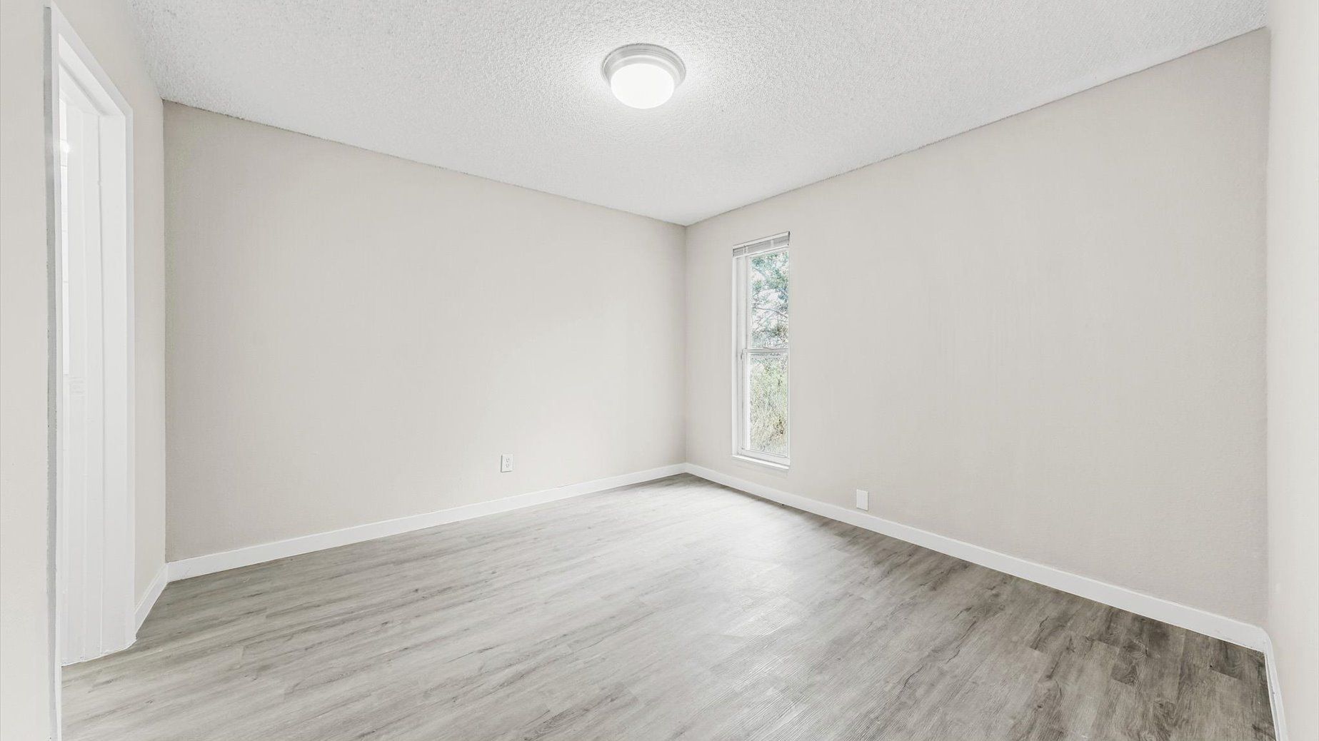Empty beige room in an apartment with a window and doorway.