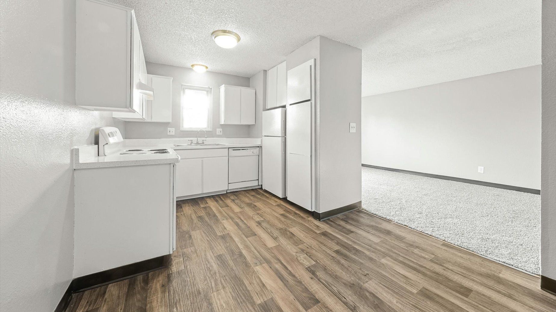 Open-concept kitchen with white cabinets and appliances, adjoining a carpeted living area.