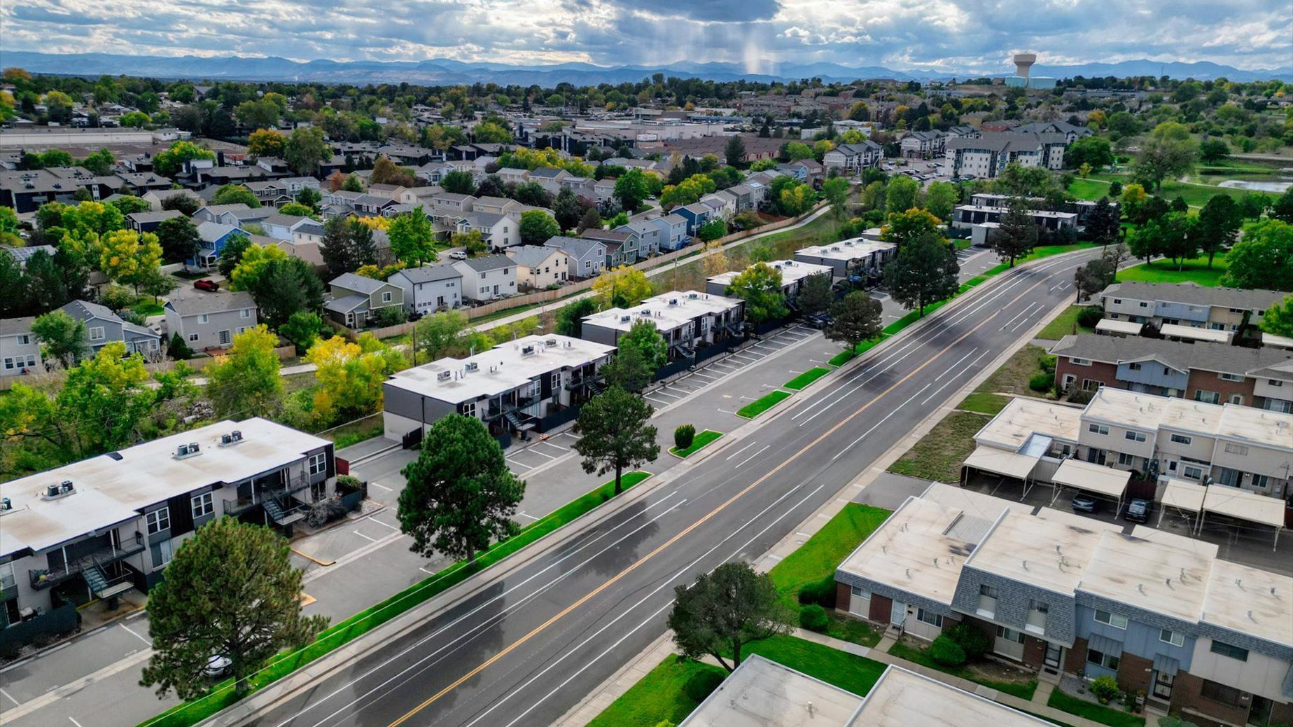Aerial view of a multi-building apartment community along a main road with green lawns and trees.
