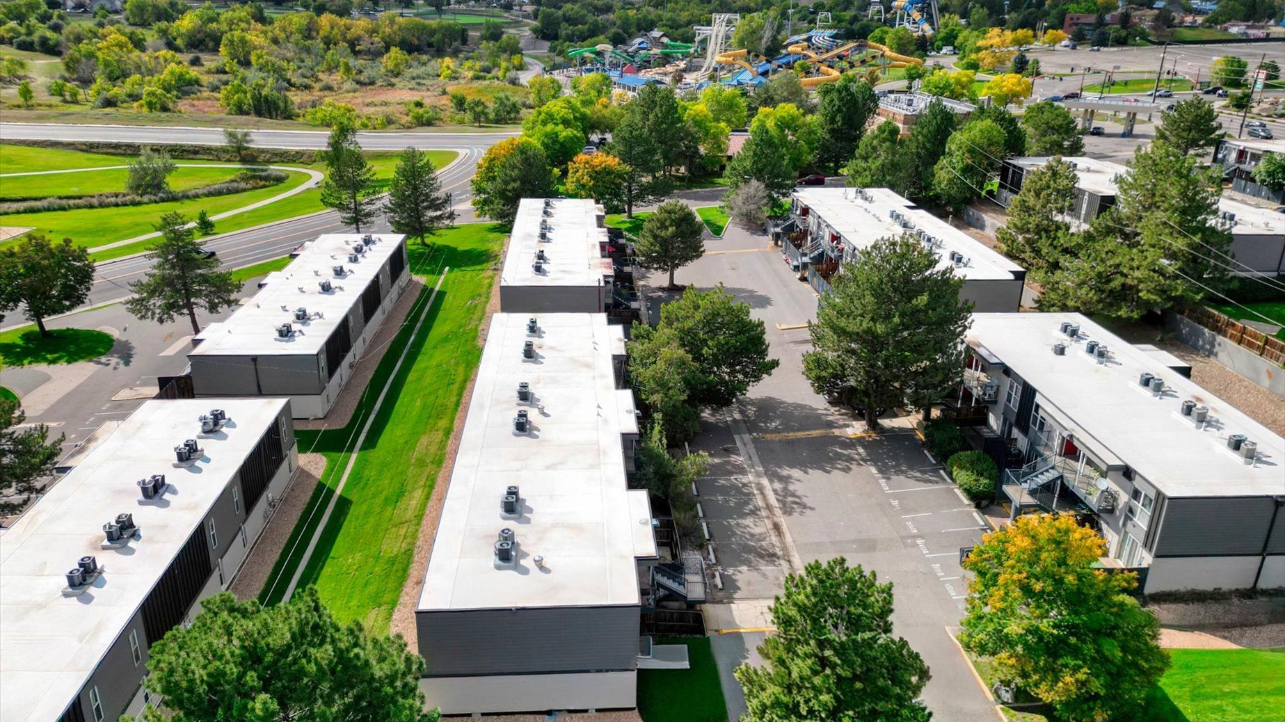 Aerial view of a modern apartment community with flat-roof buildings, trees, and parking.