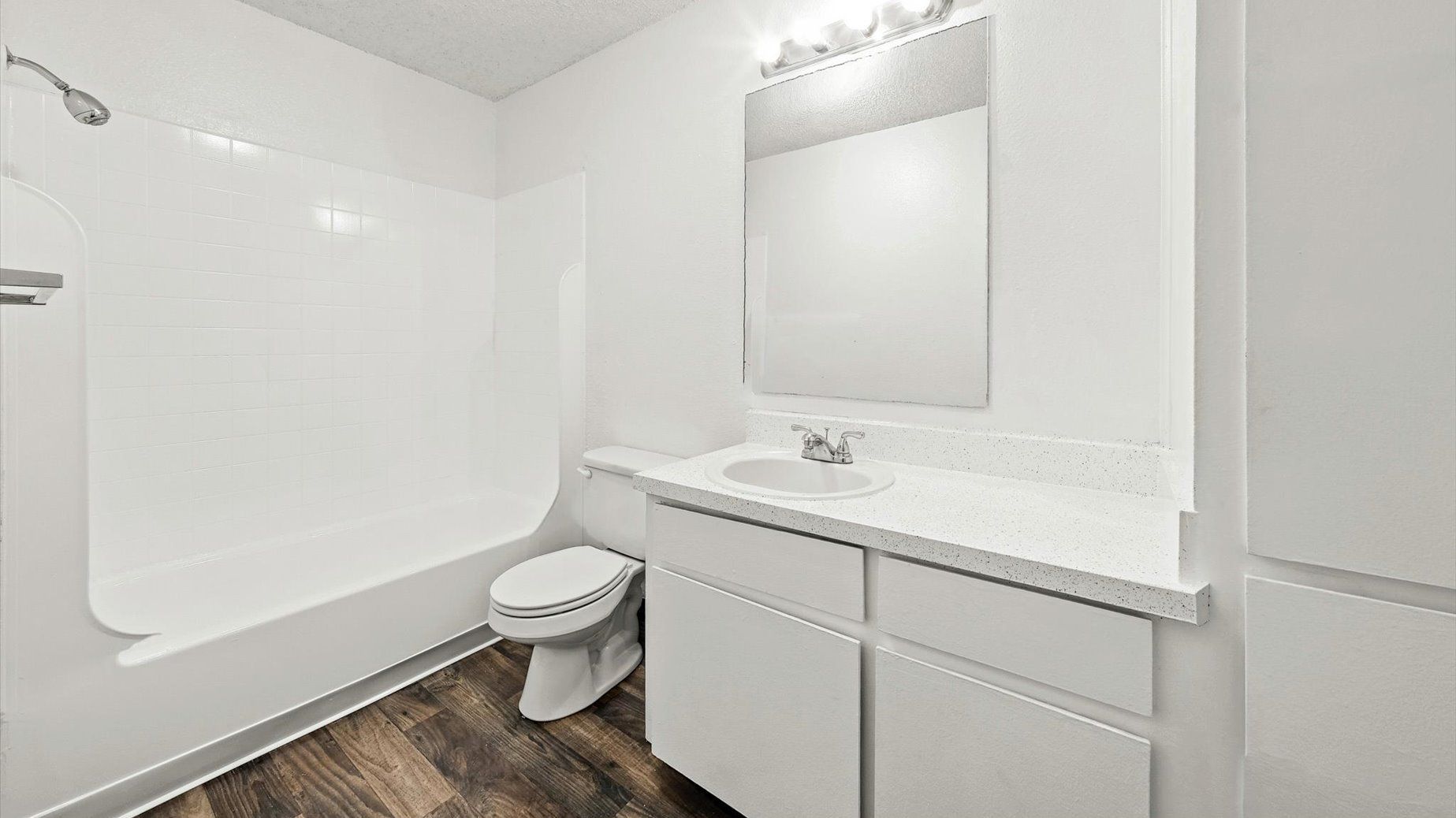 White-tiled bathroom with a bathtub/shower, toilet, and a white vanity.
