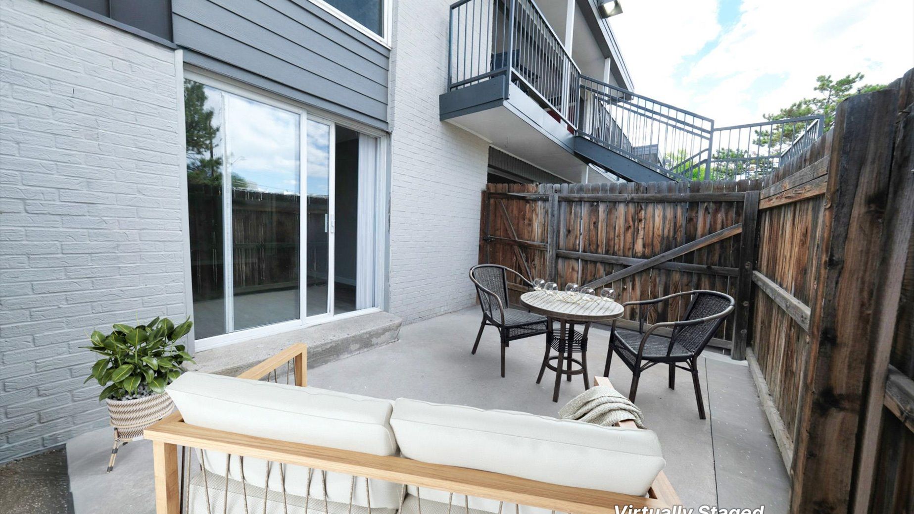 Private apartment patio with a round table, chairs, sliding glass door, and wooden fence.