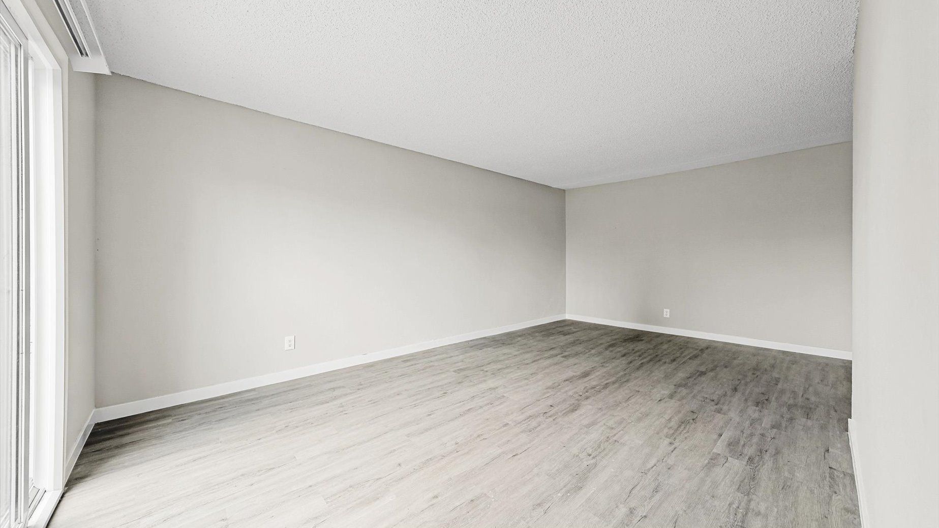 Empty living room with light gray walls, white baseboards, and a sliding glass door.