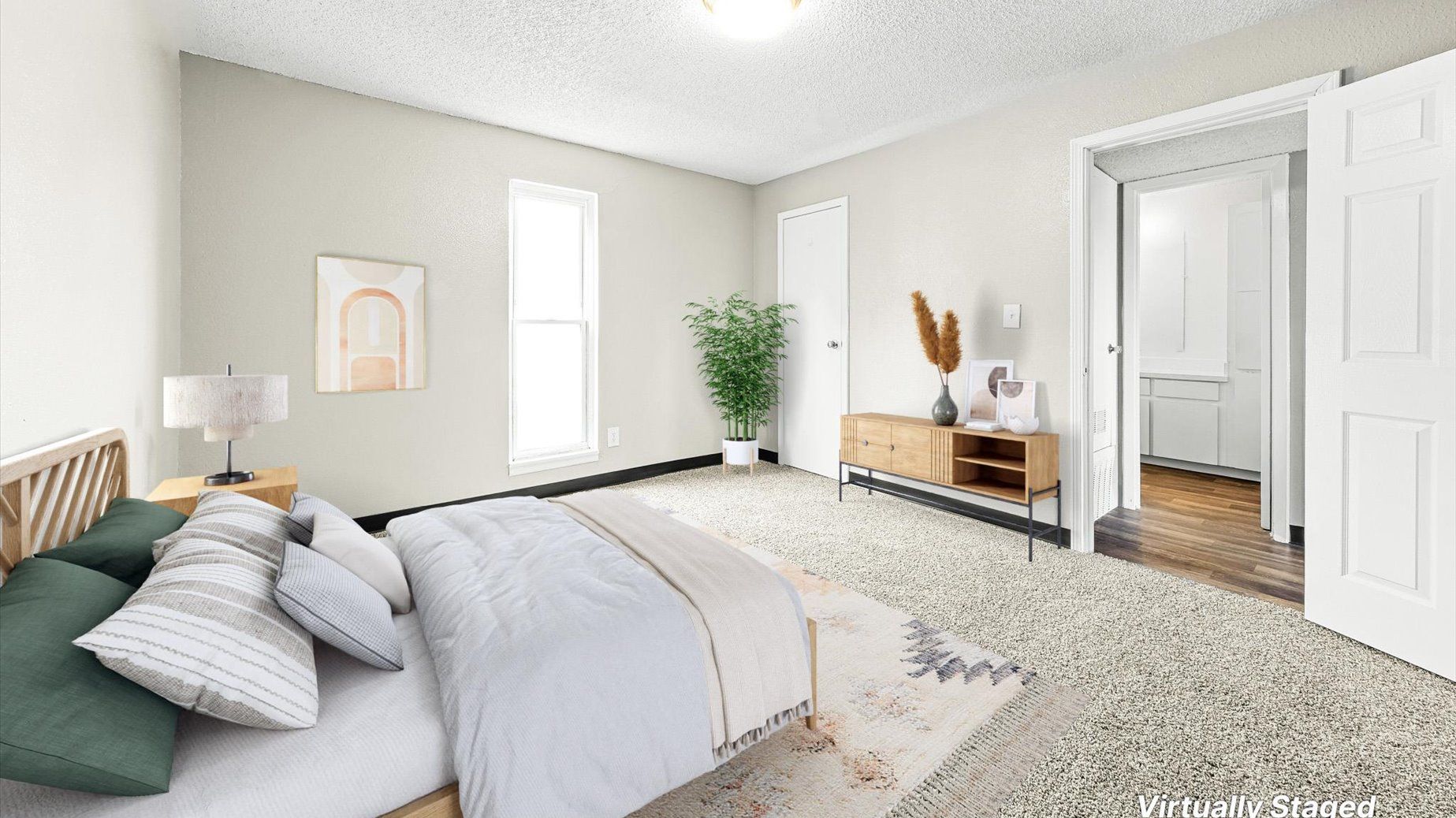 Bedroom in a virtually staged apartment with a bed, plant, and dresser.