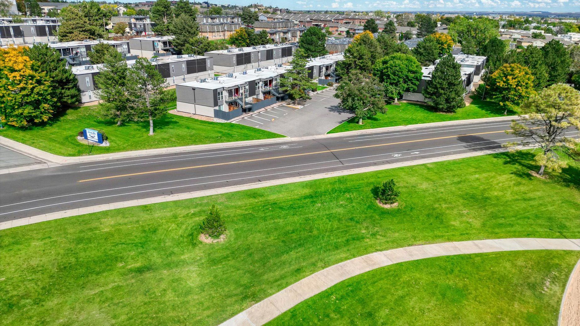 Aerial view of apartment buildings, parking, and green lawns along a street.