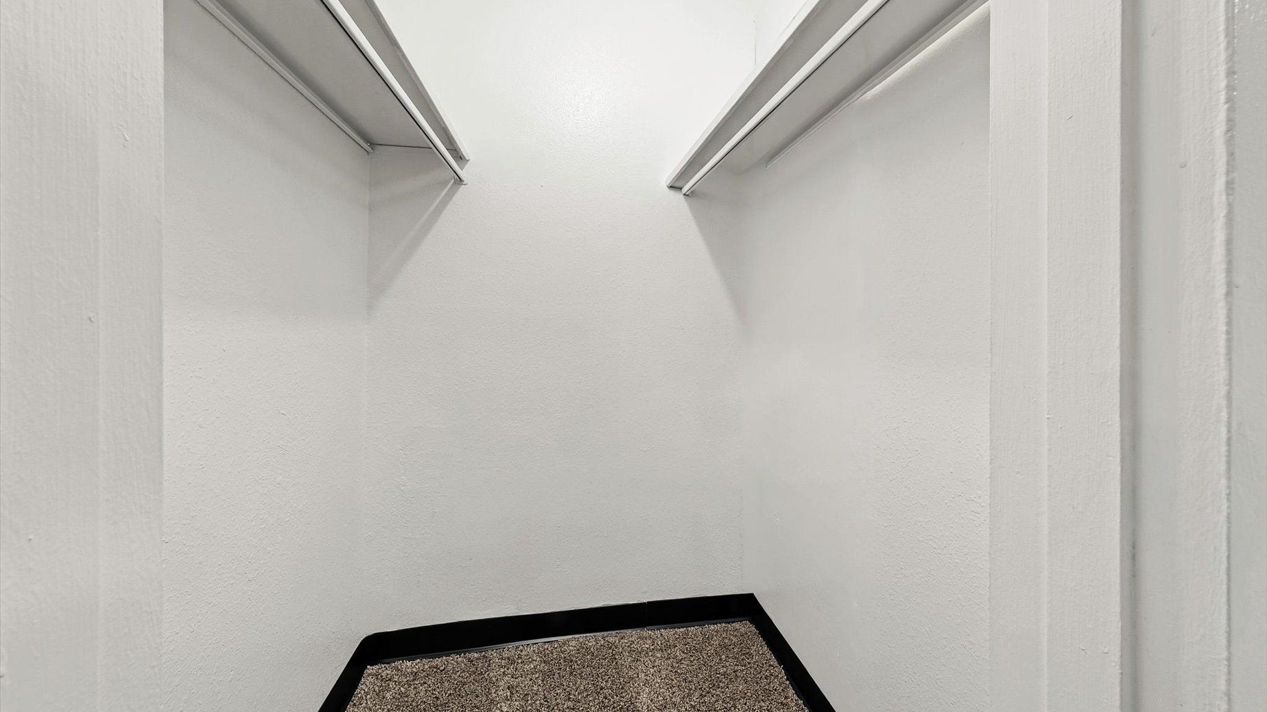 Walk-in closet with white walls and two parallel clothing rods.