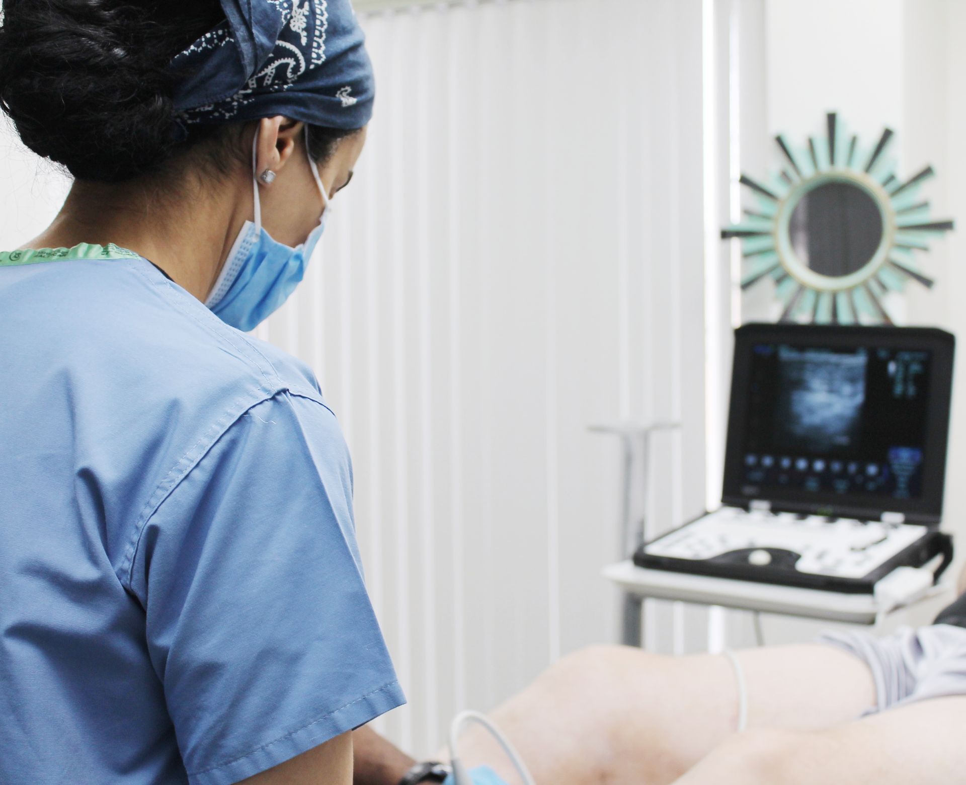 A nurse wearing a bandana and a mask looks at a patient 's leg
