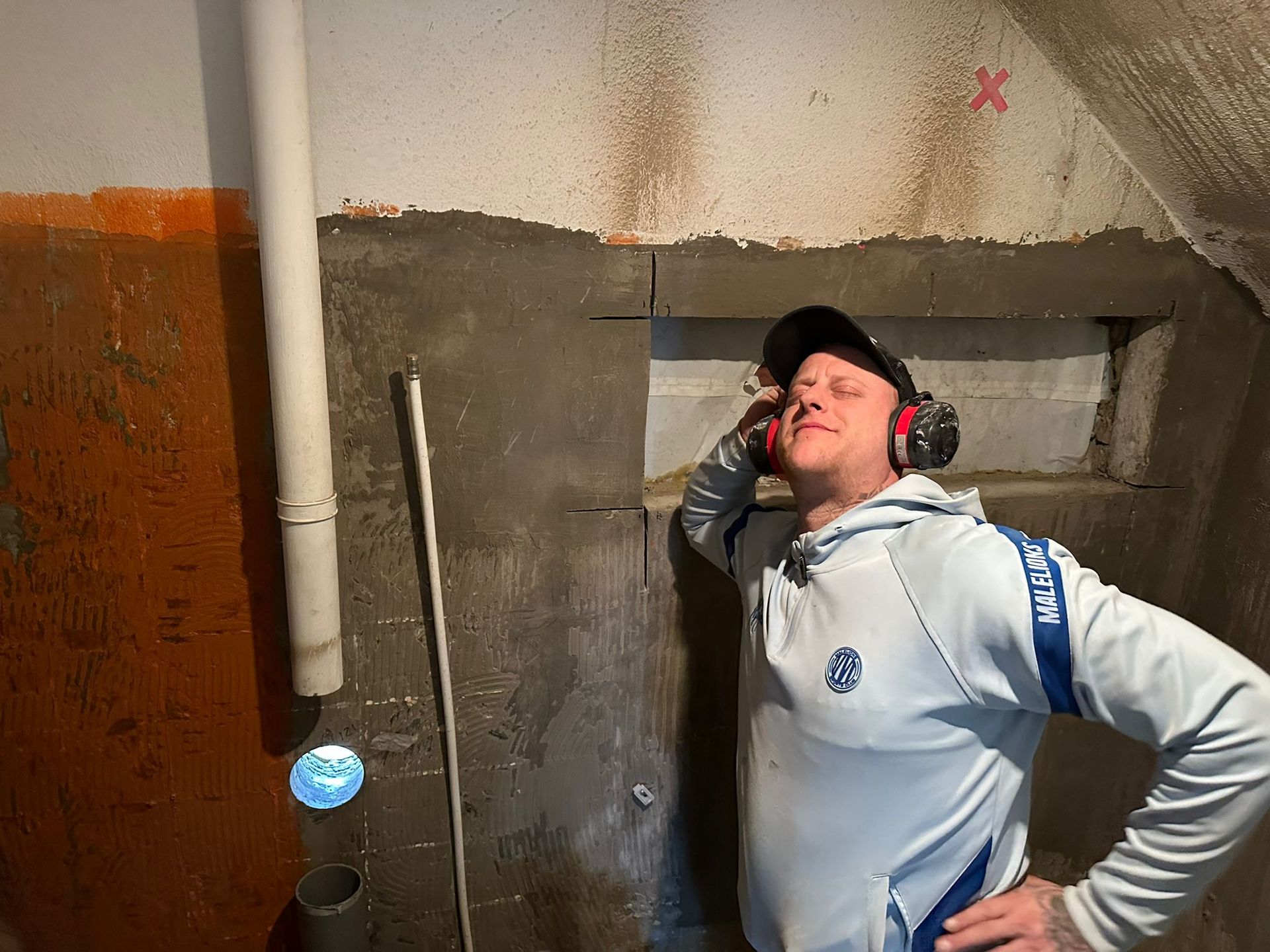 A man wearing headphones is leaning against a concrete wall with a hole in it