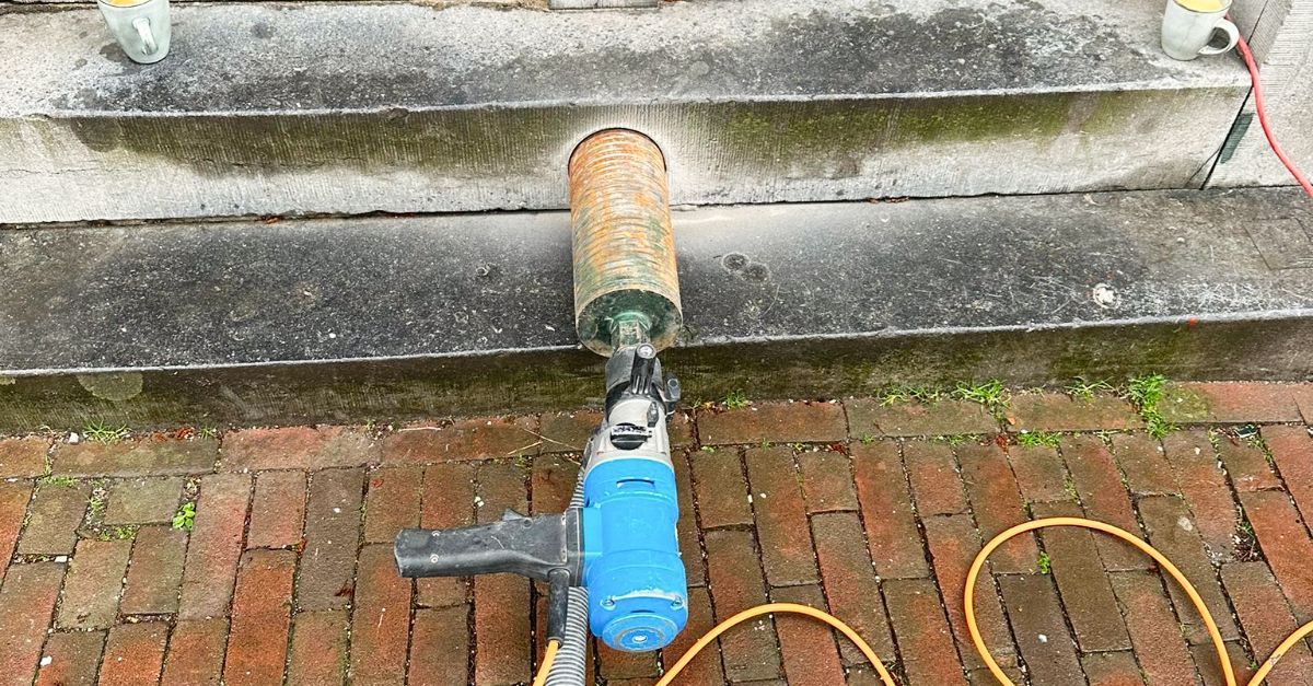 A core drill is sitting on a brick sidewalk next to a set of stairs.