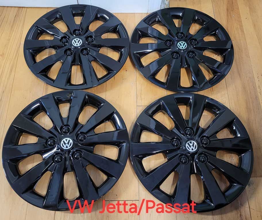 Four black Volkswagen hubcaps, likely for a Jetta or Passat, arranged on a wooden surface.