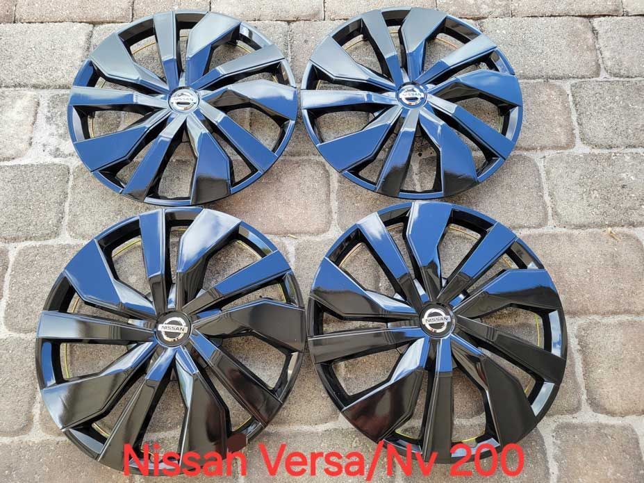 Four black and silver Nissan Versa/NV 200 hubcaps on a brick surface.