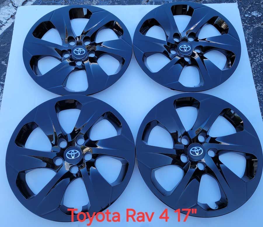 Four black Toyota Rav hubcaps with Toyota logo laid out on white surface. Four black Toyota Rav hubcaps with Toyota logo laid out on white surface.