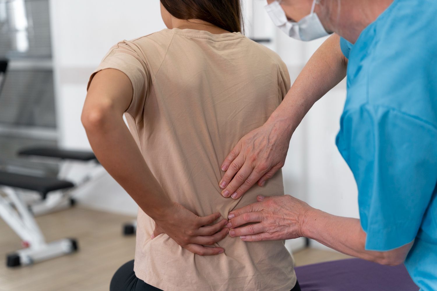 Therapist examining a patient’s lower back in a clinic, with a hand on the spine and another on the shoulder