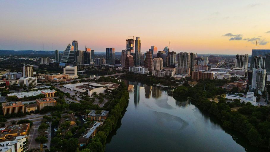 City skyline at dusk beside a calm river, with modern buildings reflecting the sunset.
