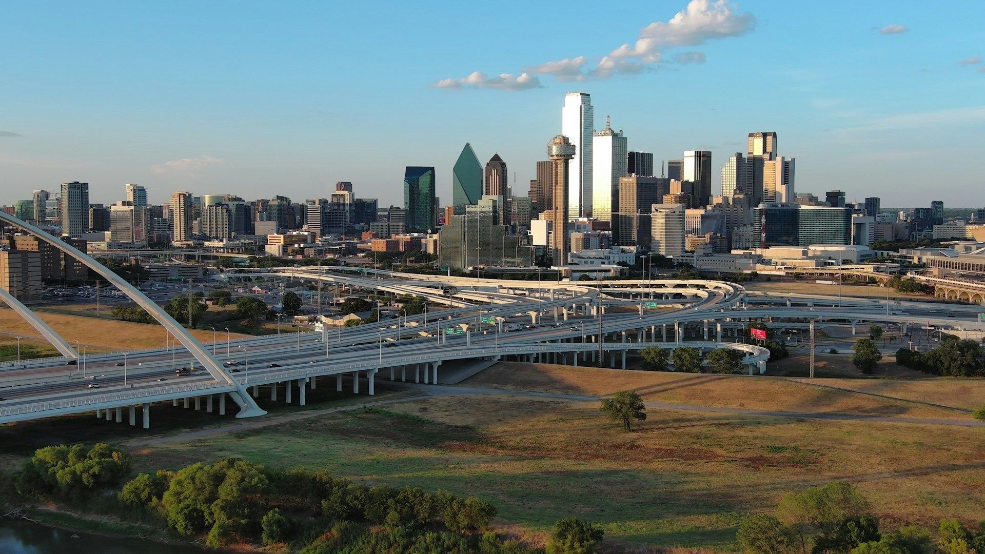 Dallas skyline with a bridge over a grassy foreground at sunset