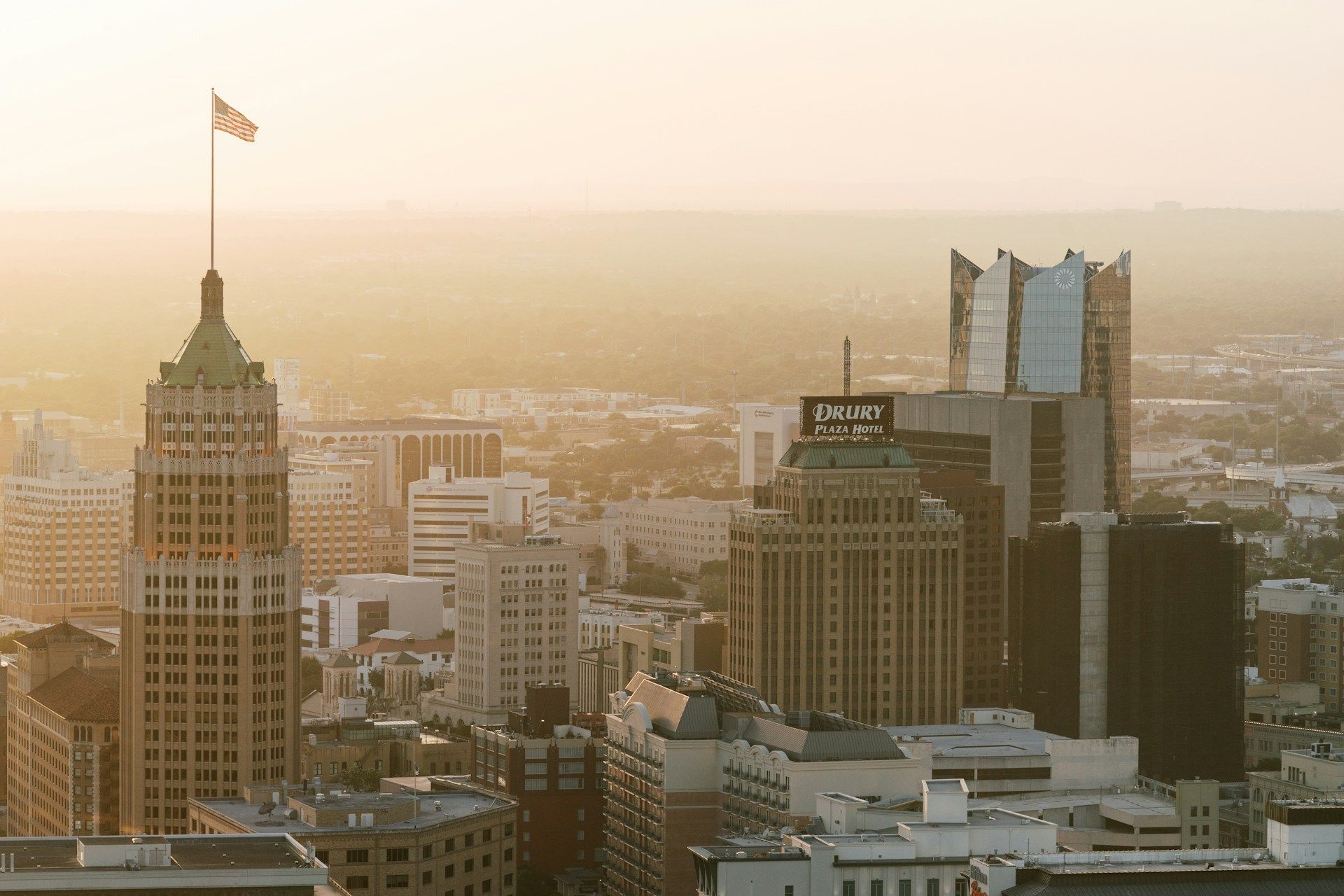 Sunlit city skyline with tall office towers and a flag-topped building at sunset