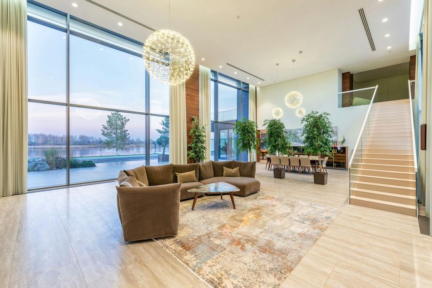 Spacious modern lobby with floor-to-ceiling windows overlooking a lake. Brown sectional, rug, and pendant light.