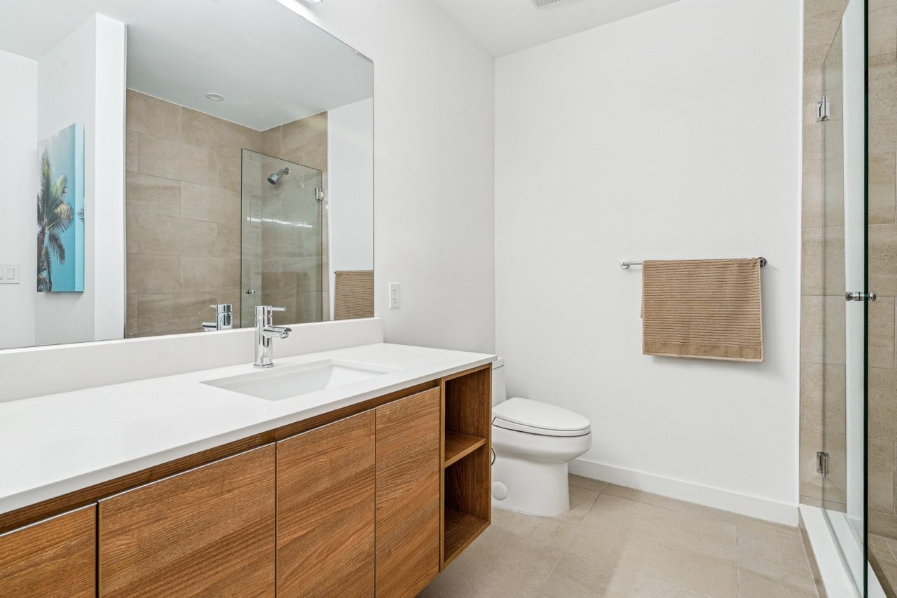 Bright bathroom with a wooden vanity, large mirror, toilet, and glass-enclosed shower.
