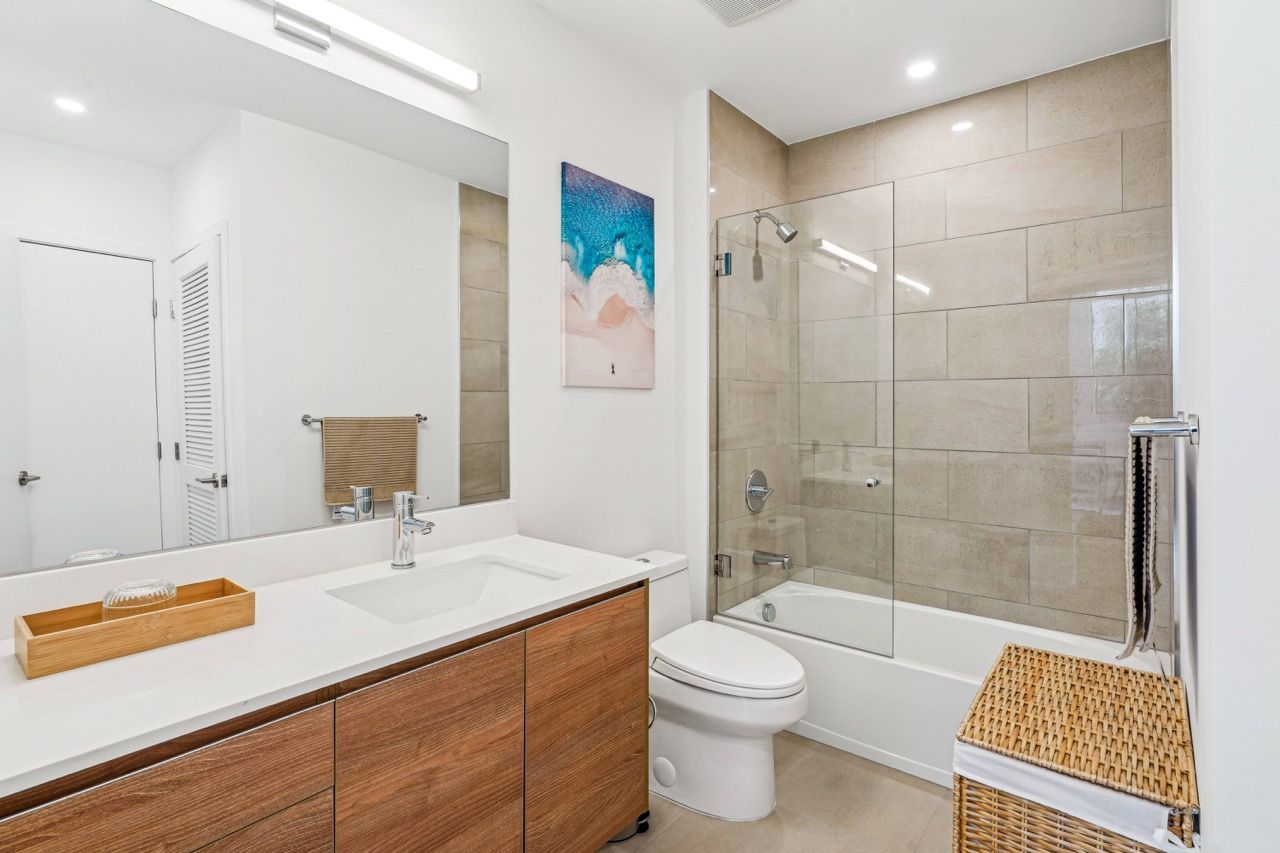 Bathroom in an apartment with a wooden vanity, sink, toilet, and glass-enclosed tub/shower.