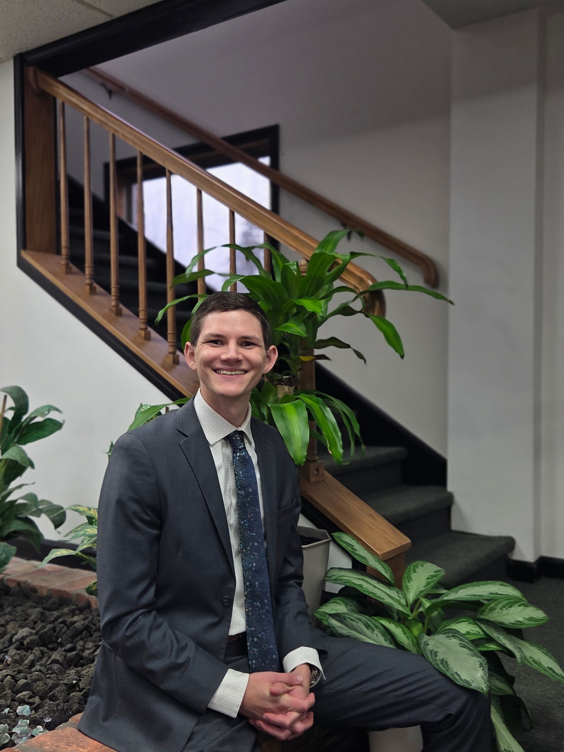 A man in a suit and tie is smiling in front of a brick wall.