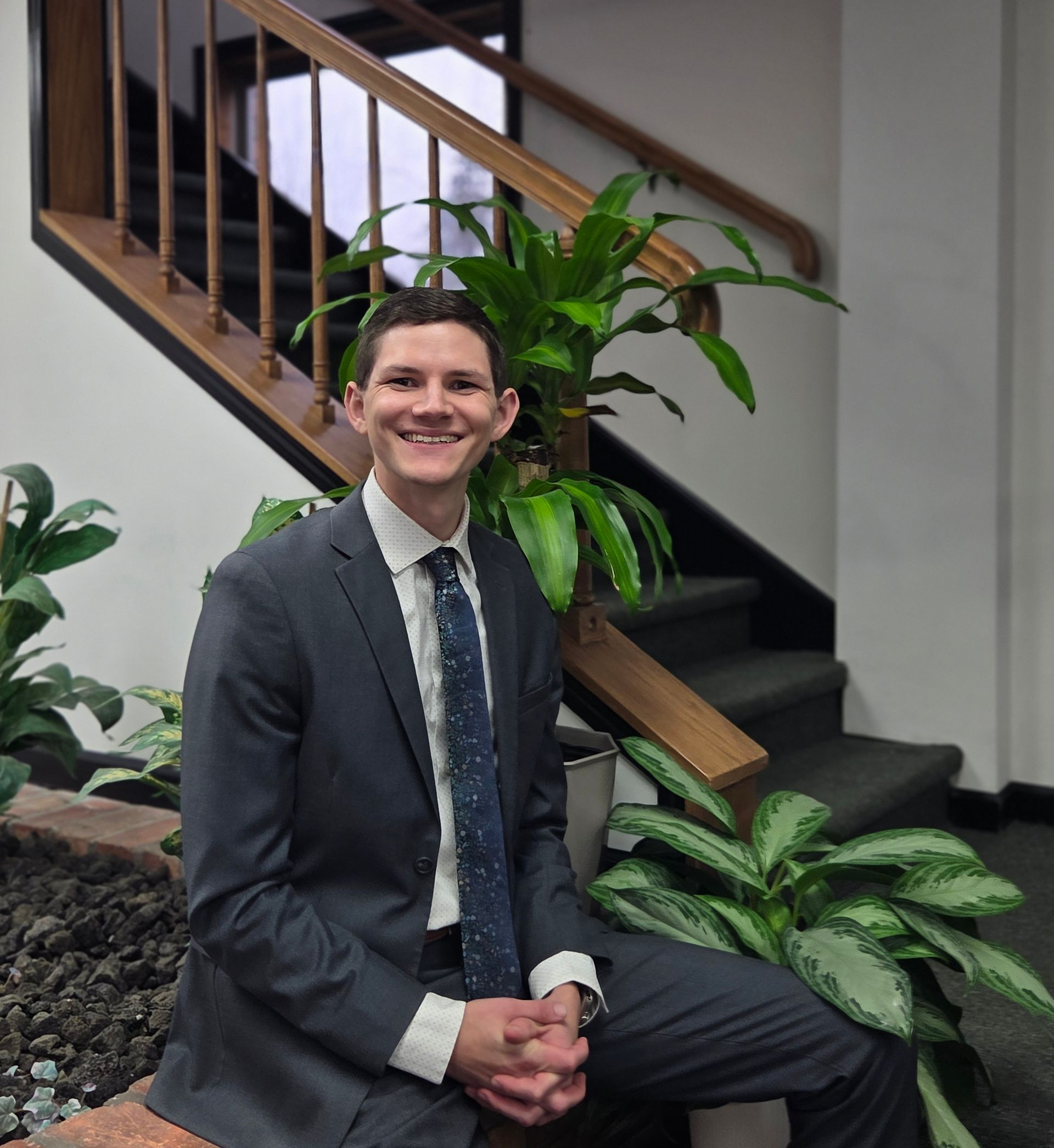 A man in a suit and tie is smiling in front of a brick wall.