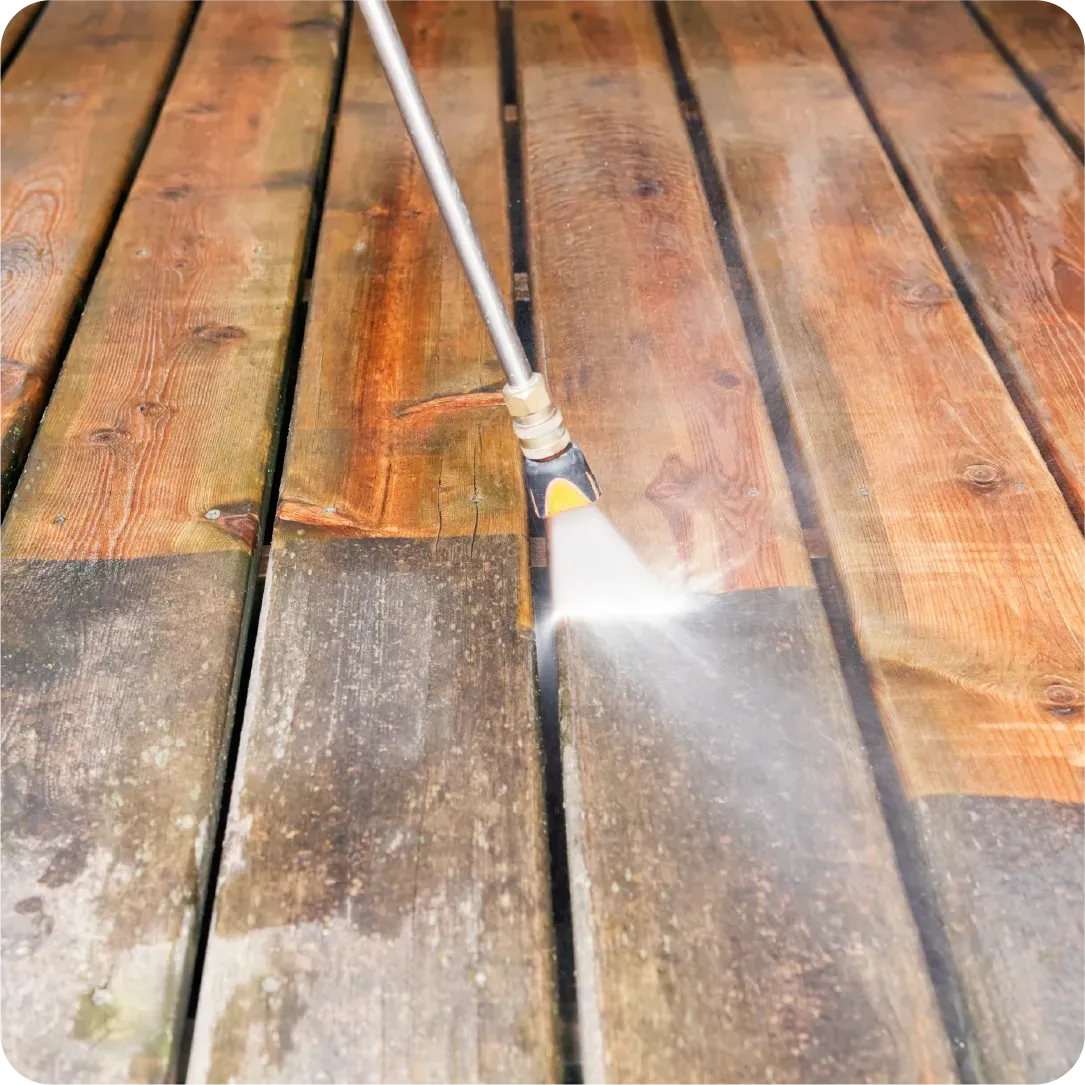 A person is cleaning a wooden deck with a high pressure washer.