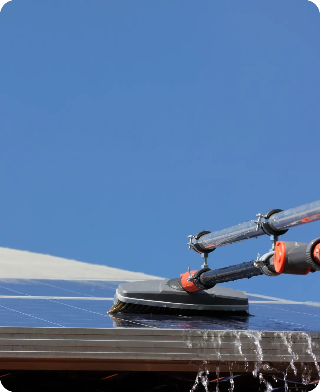 A brush is cleaning a solar panel on top of a building.