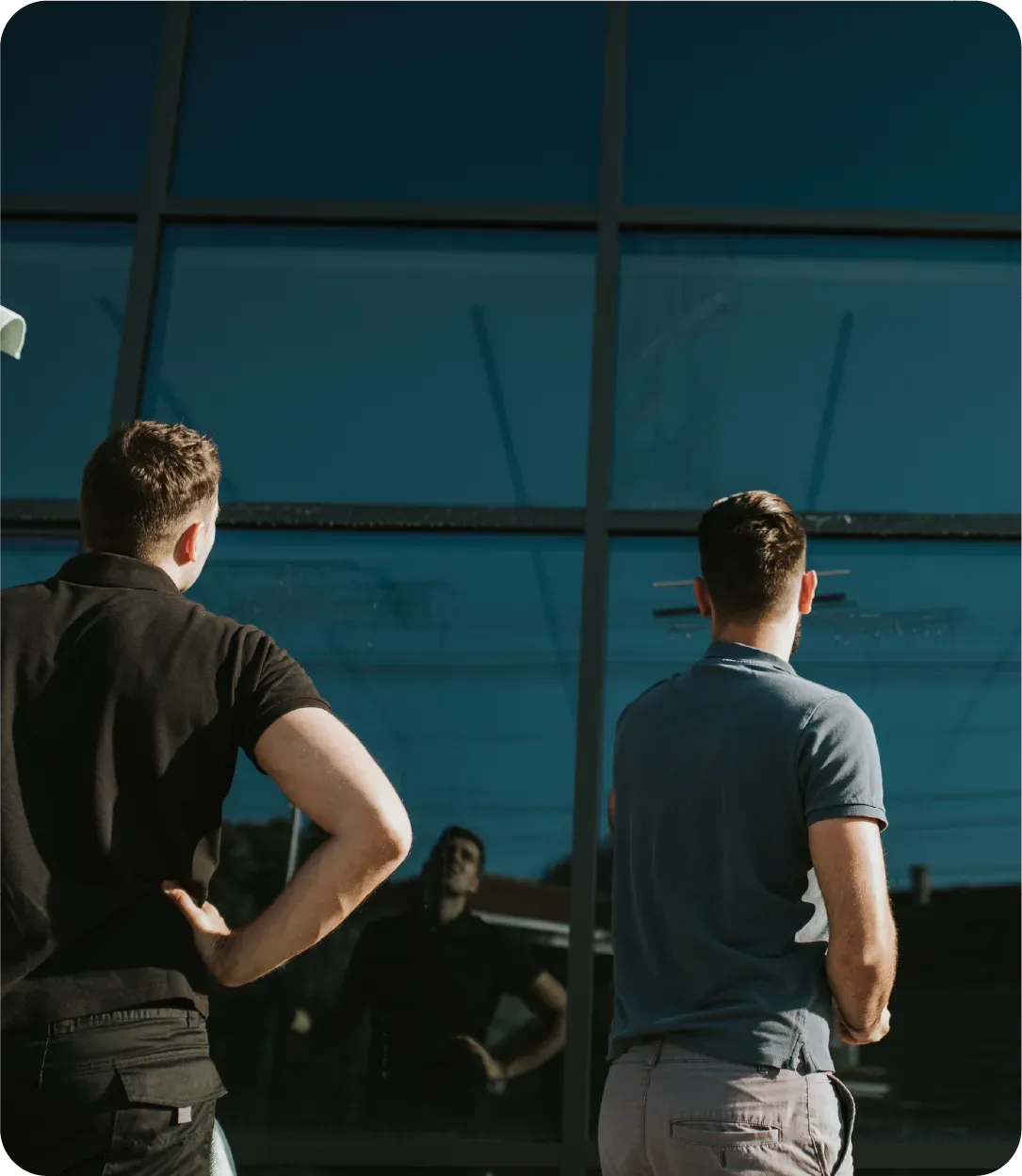 Two men are standing in front of a building looking out the window.