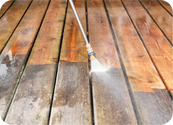 A person is cleaning a wooden deck with a high pressure washer.
