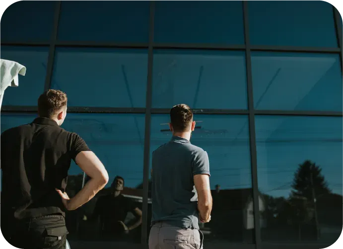 Two men are standing in front of a building looking out the window.