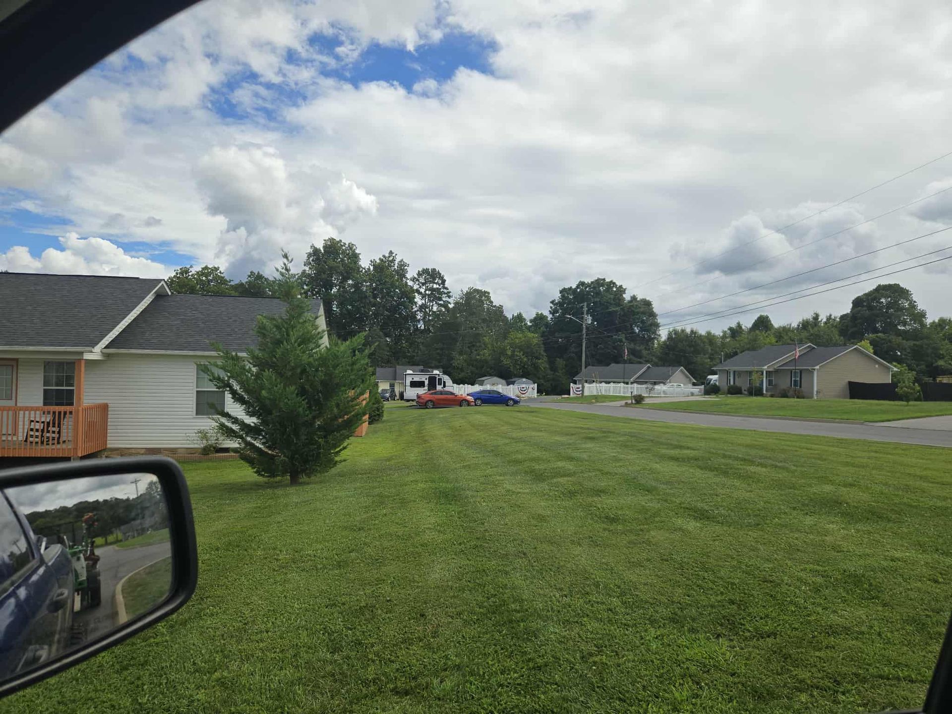 View from a car window of houses and a yard on a cloudy day.