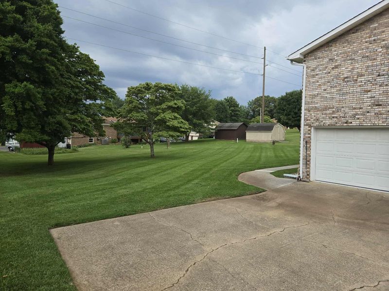 Lawn and trees in front of a house with a light-colored brick facade, overcast sky.