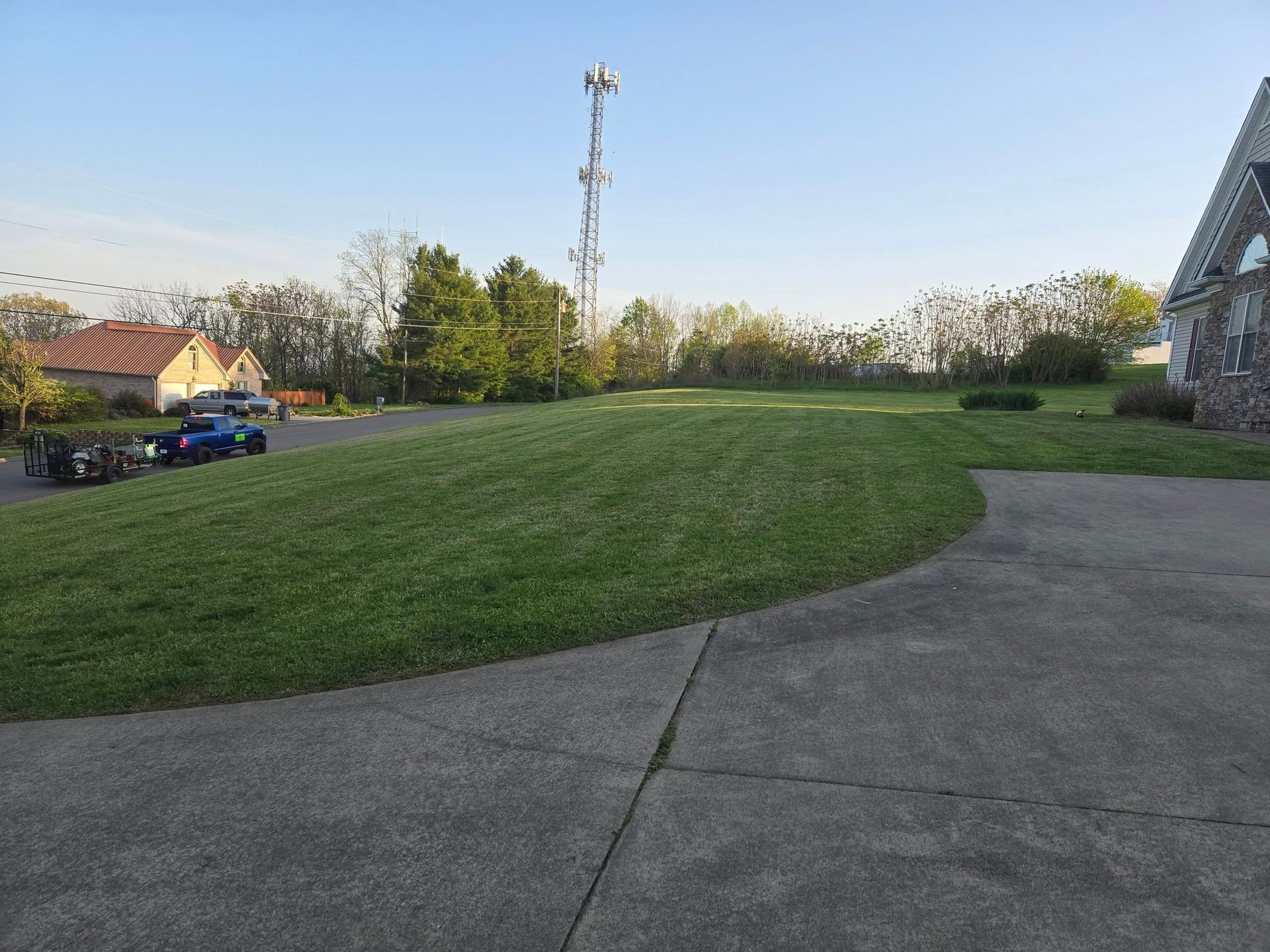 A large, green lawn next to a driveway with a cell tower in the distance.