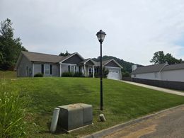 Gray house with a manicured lawn, lamp post, and blue sky.