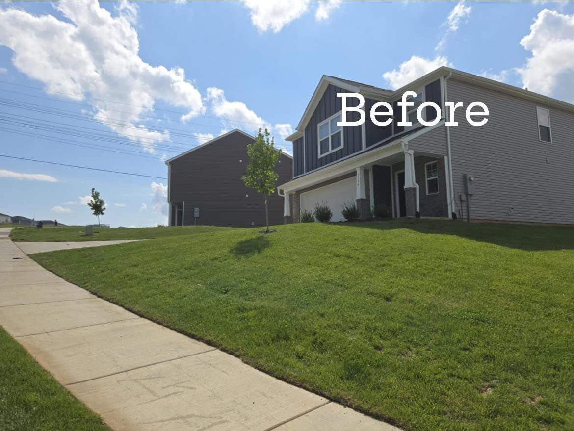 Lawn and two-story houses under blue sky; one house is gray with white garage doors, the other is brown.