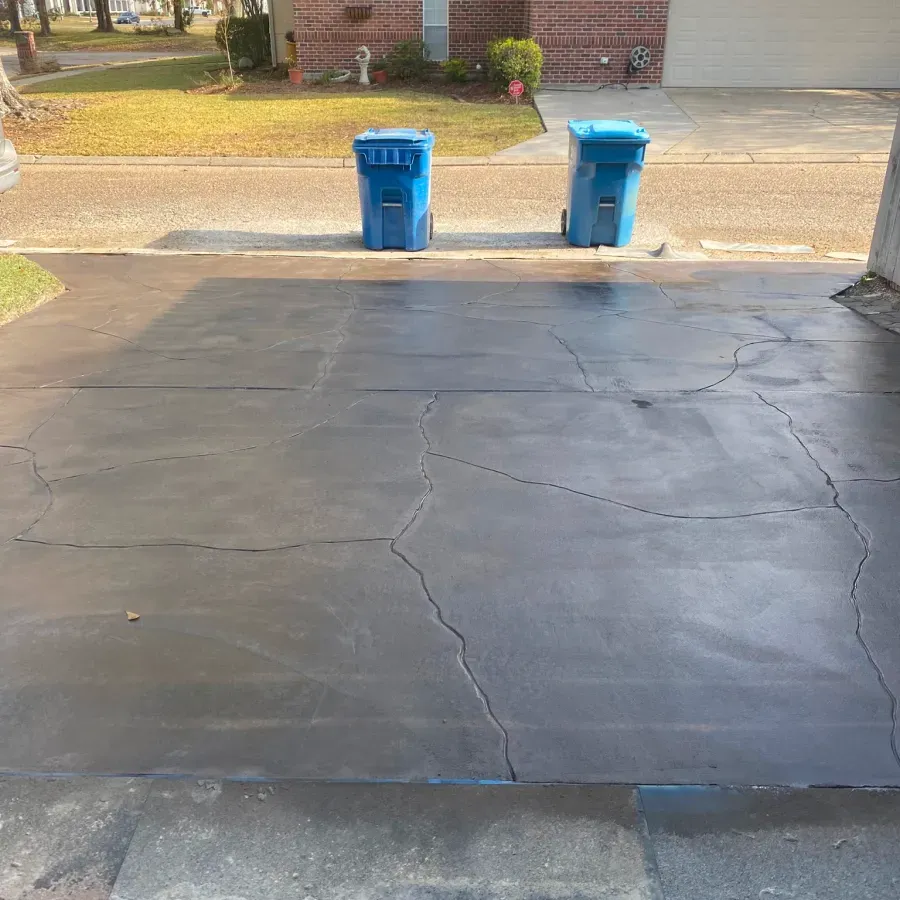 Two blue trash cans are sitting on a cracked concrete driveway.