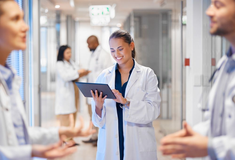 A group of doctors are standing in a hospital hallway looking at a tablet.