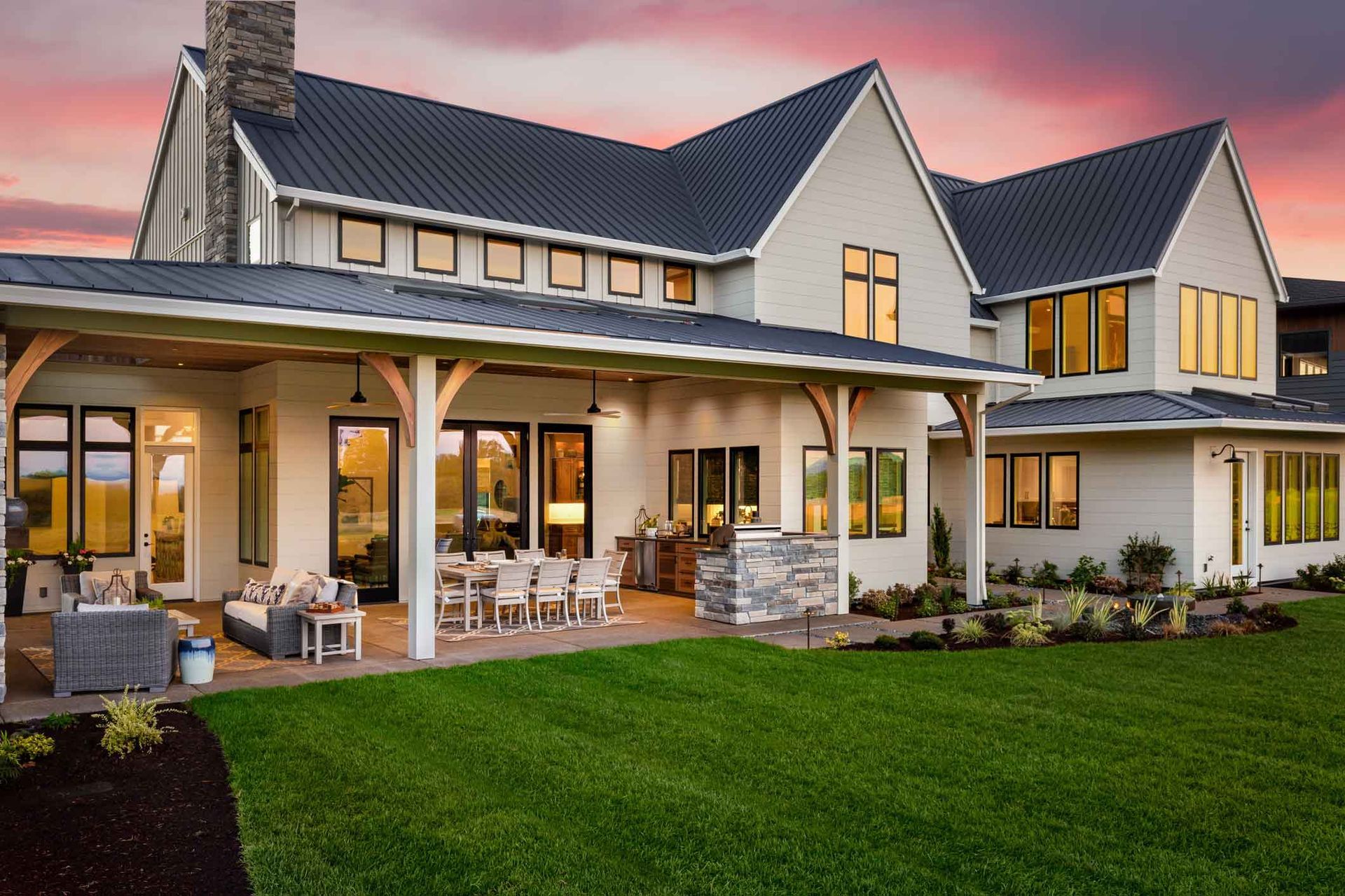 Large modern house with a covered porch, stone accents, and a green lawn at sunset