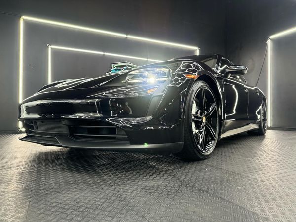 A black porsche taycan is parked in a garage.