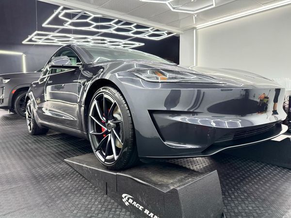 A tesla model 3 is parked on a ramp in a garage.
