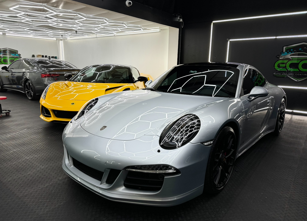 A silver porsche 911 is parked next to a yellow sports car in a garage.