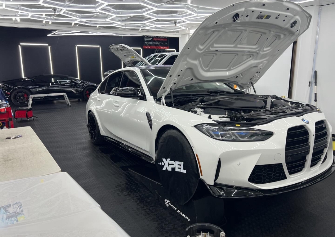 A white bmw m3 is parked in a garage with the hood open.