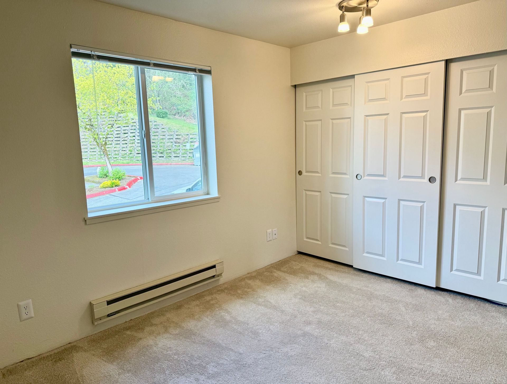 An empty bedroom with a window and sliding closet doors.