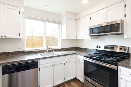 A kitchen with white cabinets , stainless steel appliances , a stove , dishwasher , and microwave.